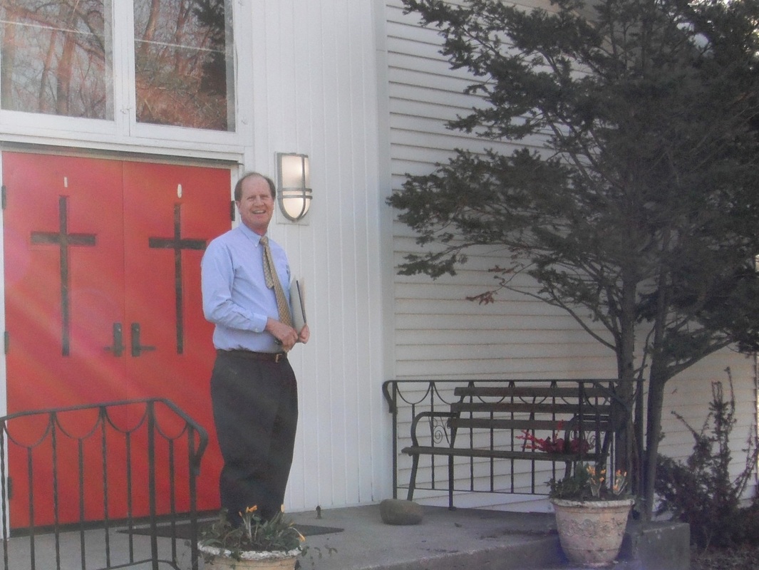 Man dressed for church standing in front of red church doors